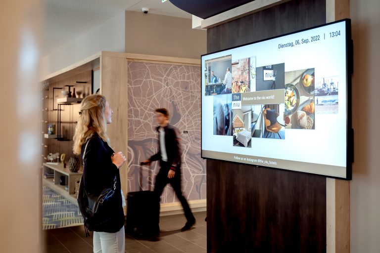 Hotelgästin blickt auf Digital Signage Screen in der Lobby